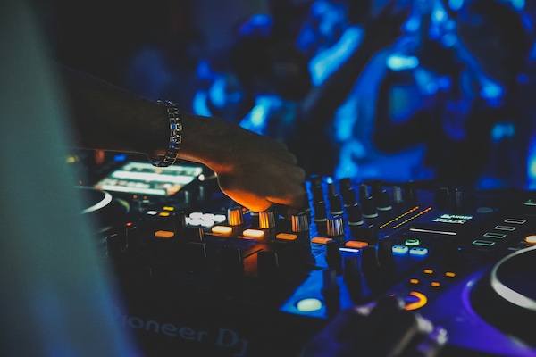 DJ hand on Pioneer mixer with waveform screen glowing in dark club