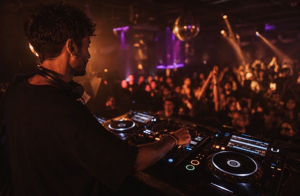 how to get a DJ residency — DJ performing a club set behind CDJs with crowd in the background