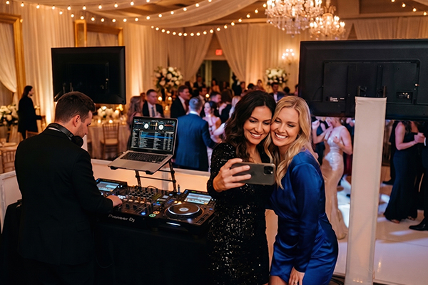 Two women using Ribalta's photobooth service with phone at a wedding DJ booth
